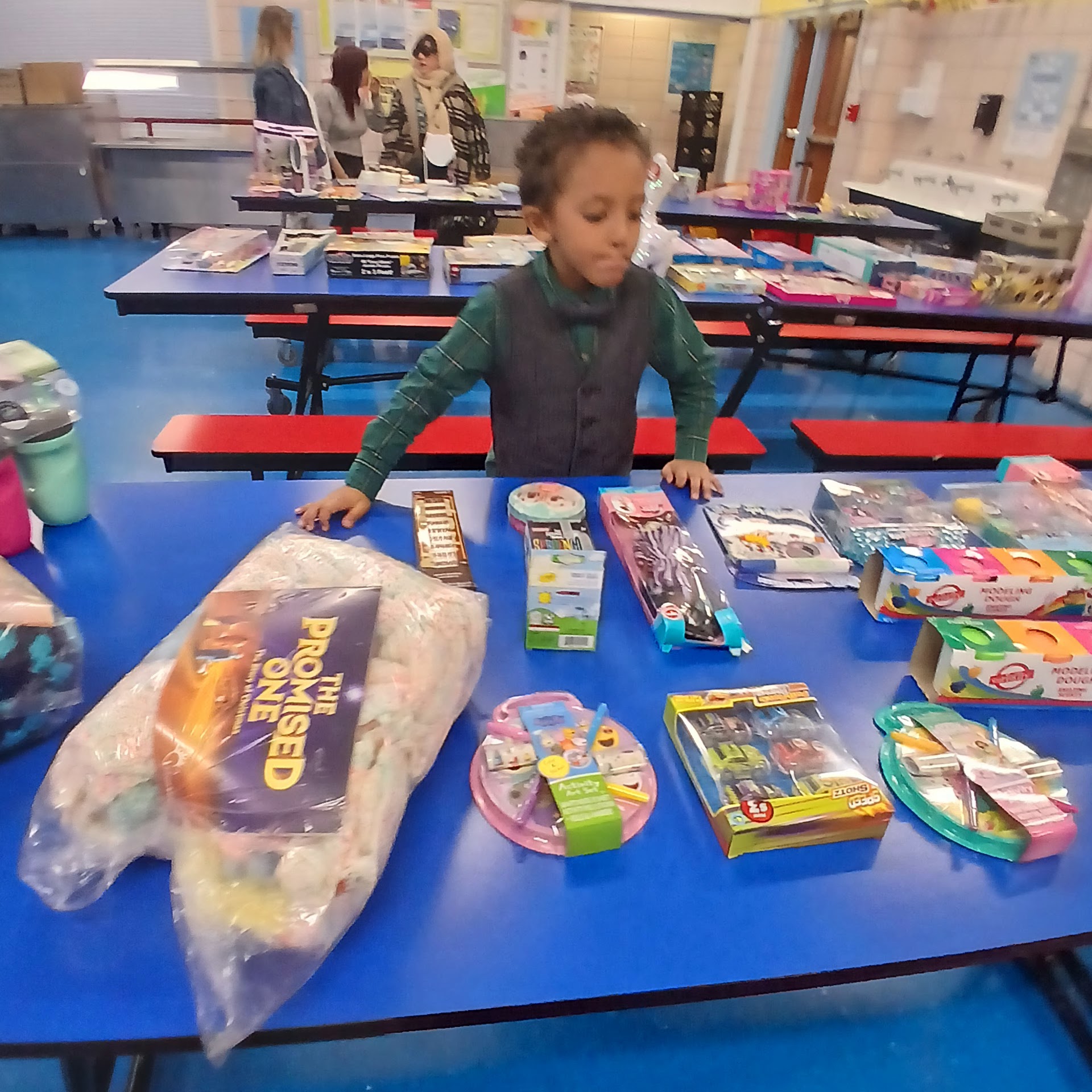 Child standing beside tables of toys while holding a selected gift box